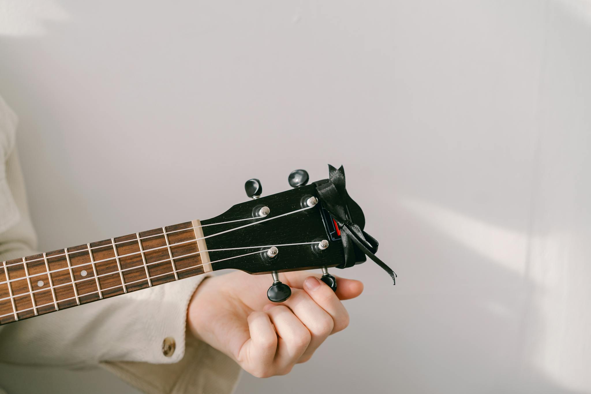 A detailed close-up of a person tuning a ukulele against a plain background.