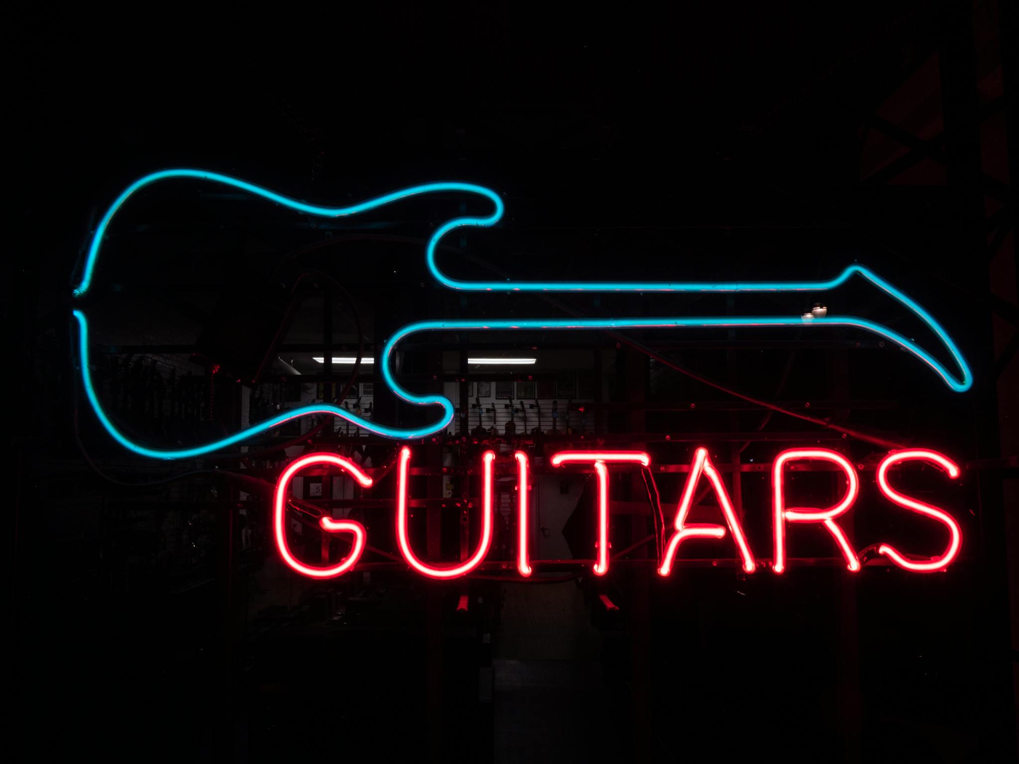 Electric guitar neon sign glowing in the dark, showcasing vibrant blue and red colors.