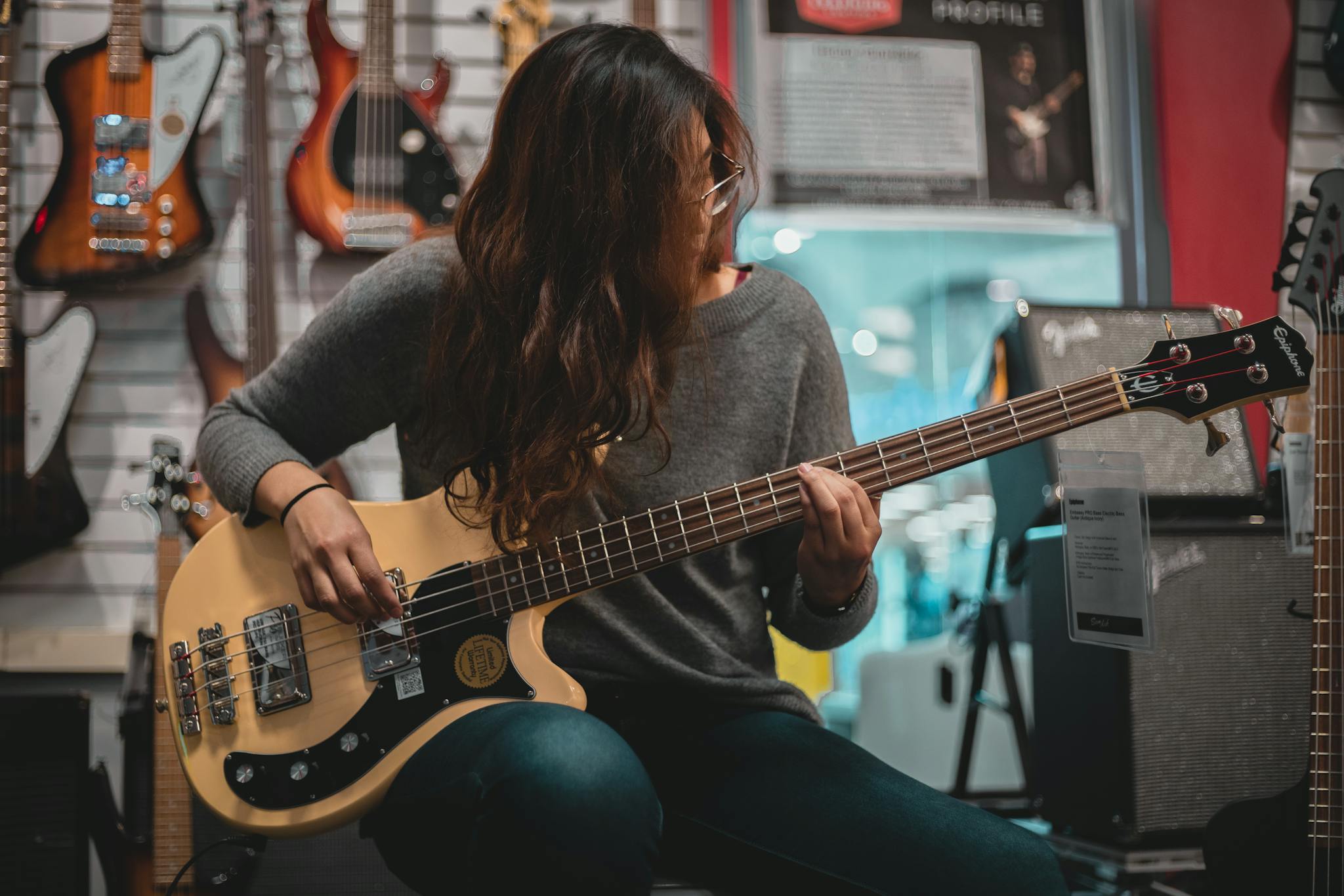 Woman playing an electric bass guitar in a music shop, surrounded by guitars.